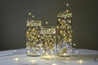 Three glass containers with star decorations and string lights on a dark background